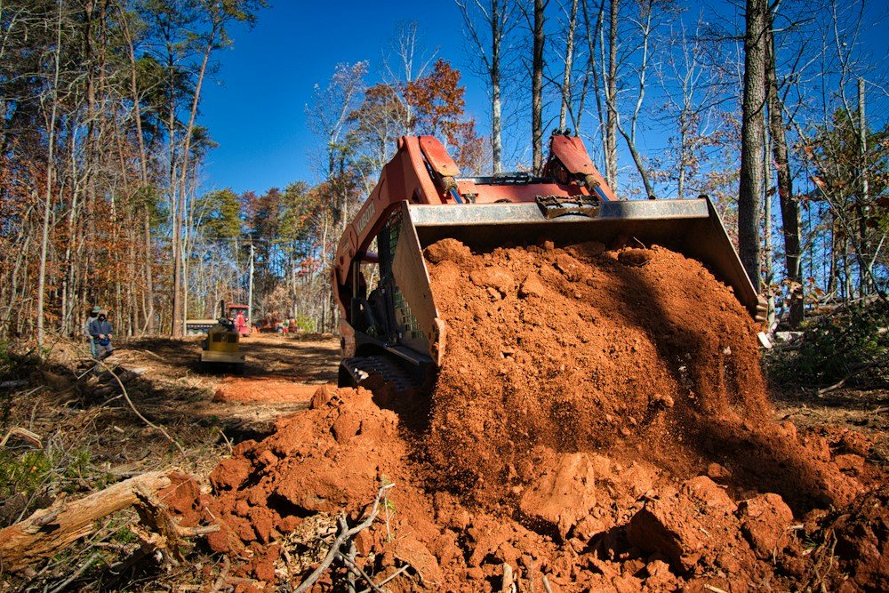 A skid steer pushing cleared brush into a pile on a wooded lot